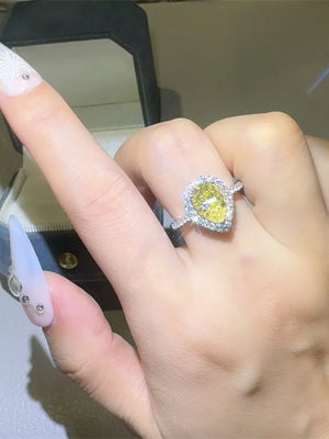 Yellow pear-cut moissanite ring with halo of small diamonds on a silver band.