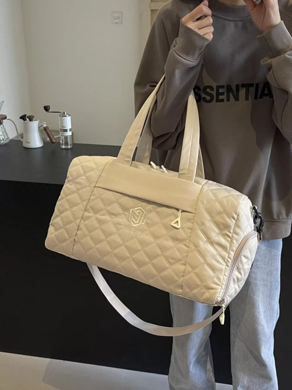 Diamond-stitched beige quilted duffel bag with adjustable strap and front zip pocket.