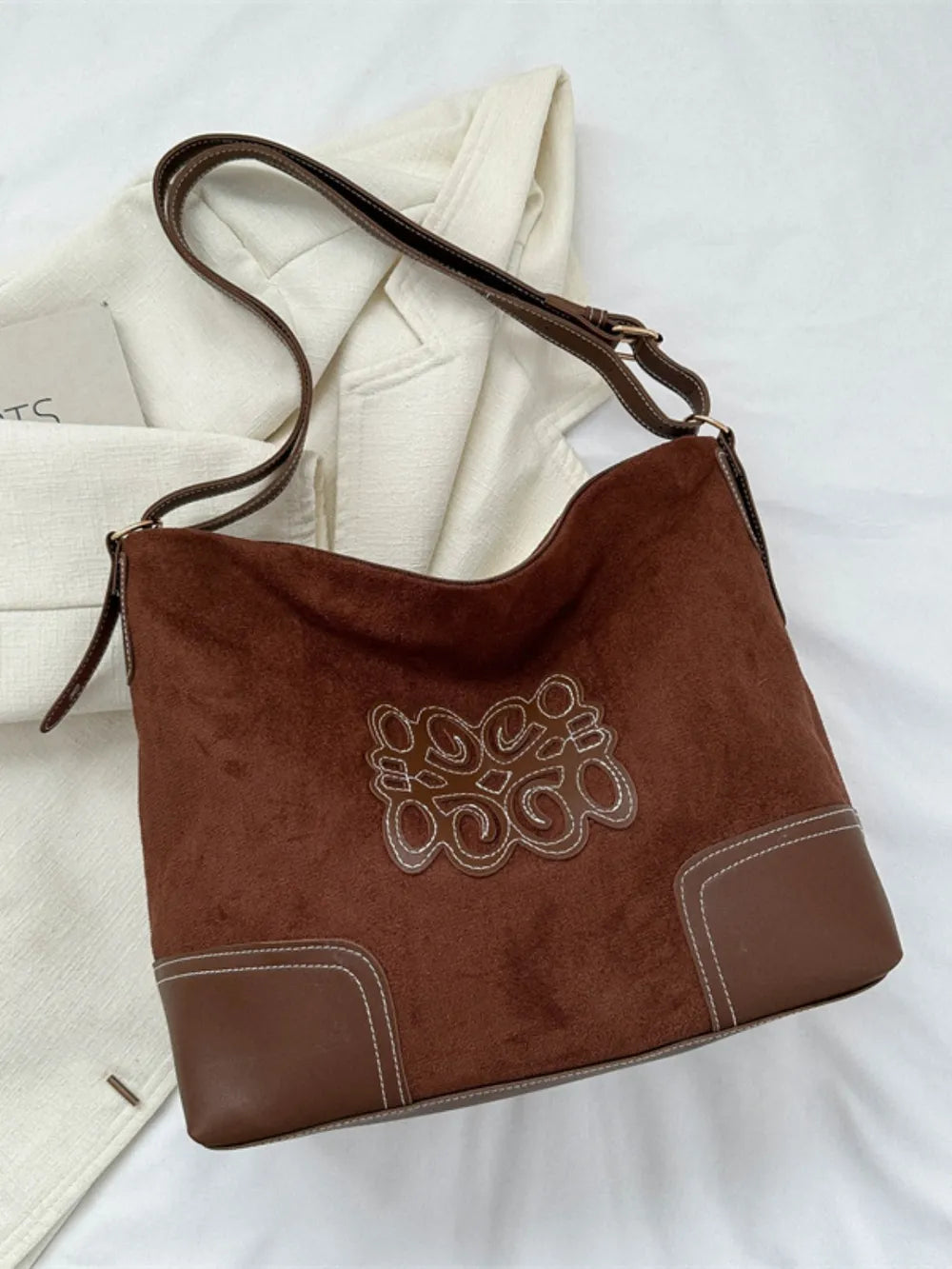 Dark brown suede hobo bag with contrast stitching and appliqué detail.