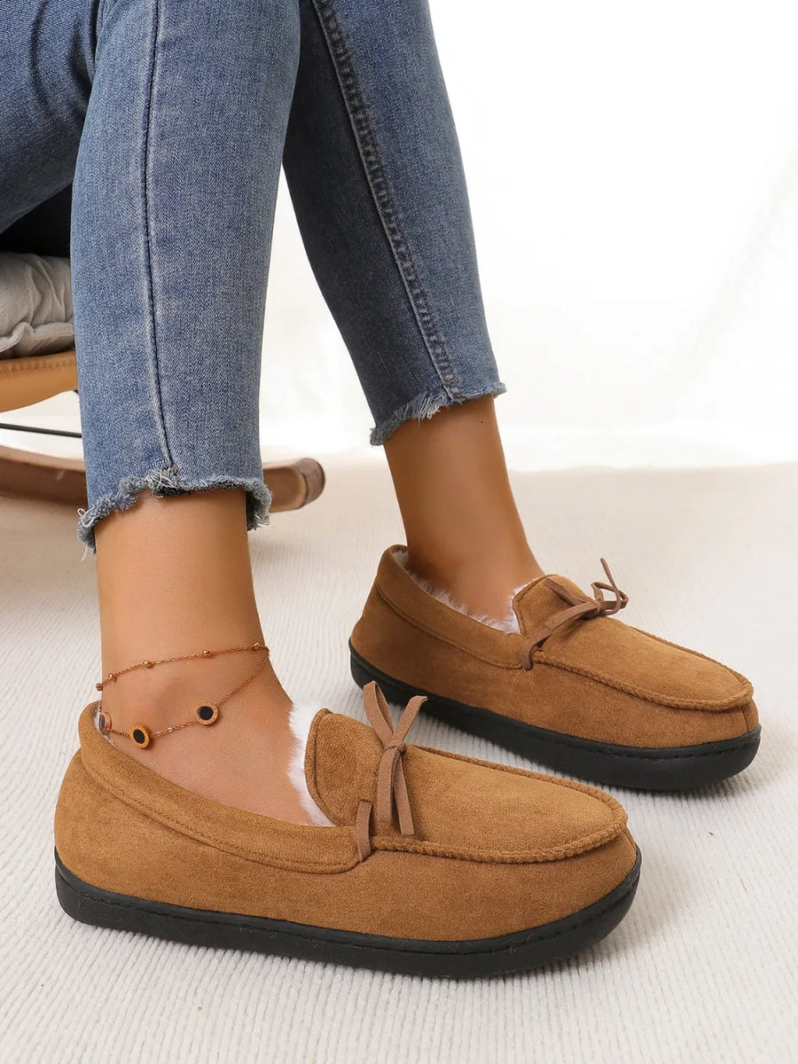 Caramel suede moccasin slippers with white faux fur lining and a bow detail.