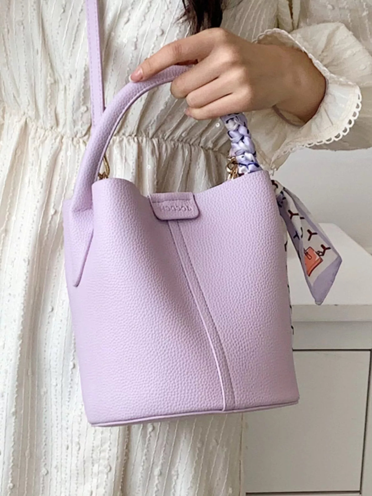 Chic purple bucket crossbody bag with decorative scarf detail and top handle.