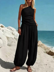 Black one-shoulder top and wide-leg pants set with draped detail, styled with sandals.