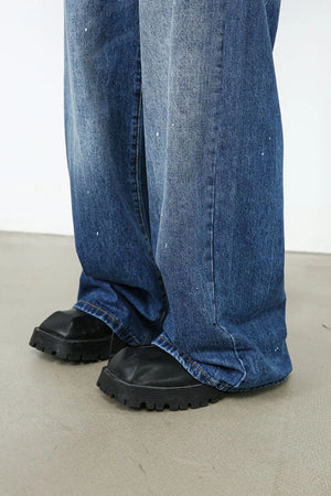Painterly denim palazzo trousers in medium wash with white paint splatters and wide leg.