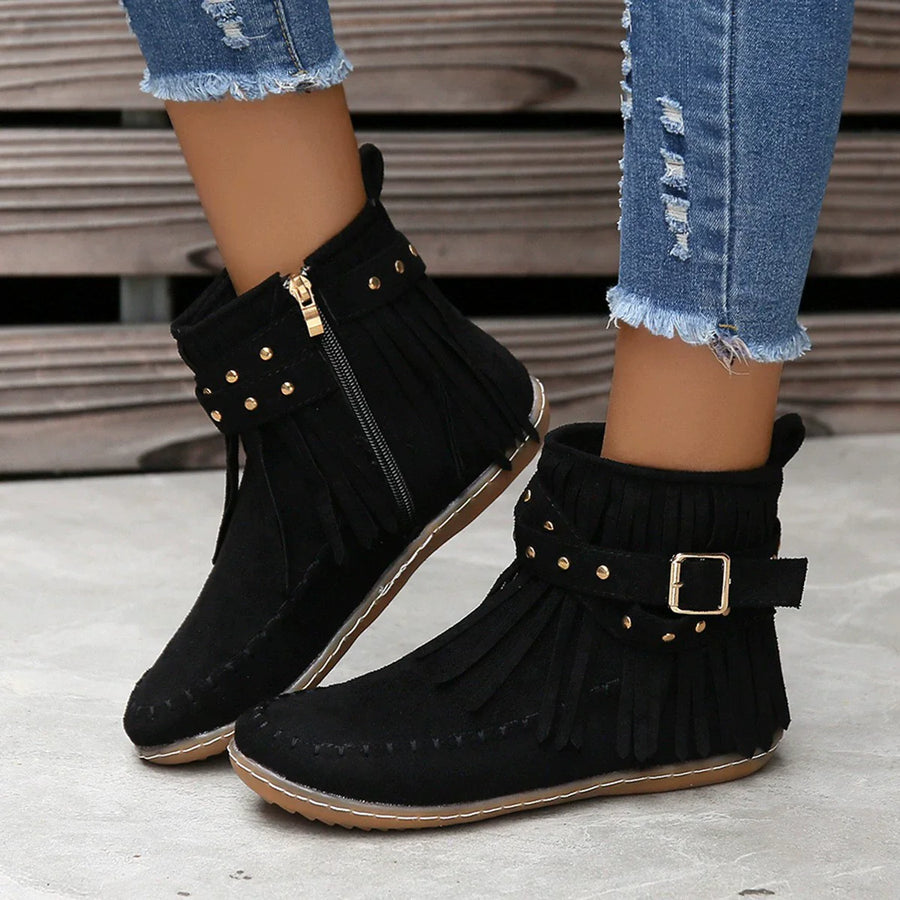 Black suede ankle boots with fringe, studs, and buckle detail.