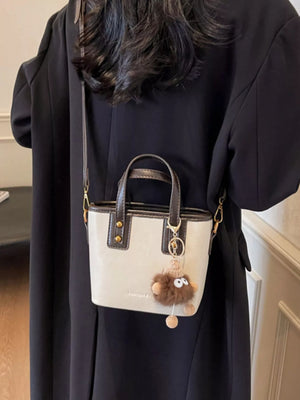 Mini leather crossbody bag in beige with brown trim and a fluffy charm detail.