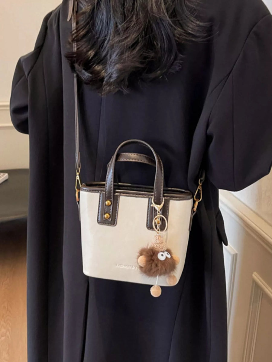 Mini leather crossbody bag in beige with brown trim and a fluffy charm detail.
