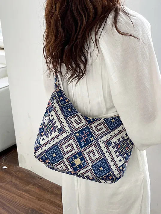 Blue embroidered geometric hobo bag with artistic pattern.