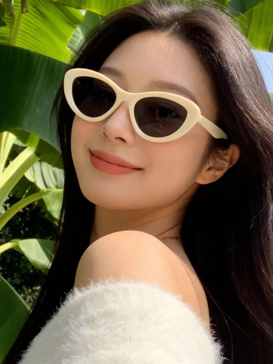 Ivory cat eye sunglasses with dark lenses, worn by a woman outdoors.