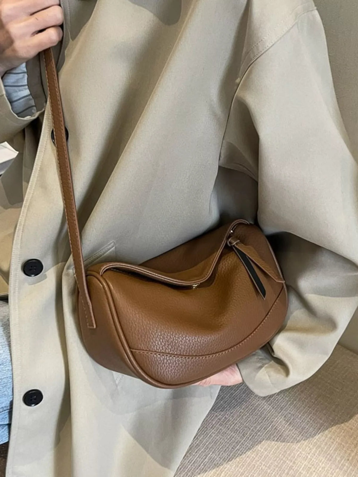 Brown leather minimalist crossbody bag with a curved shape and adjustable strap