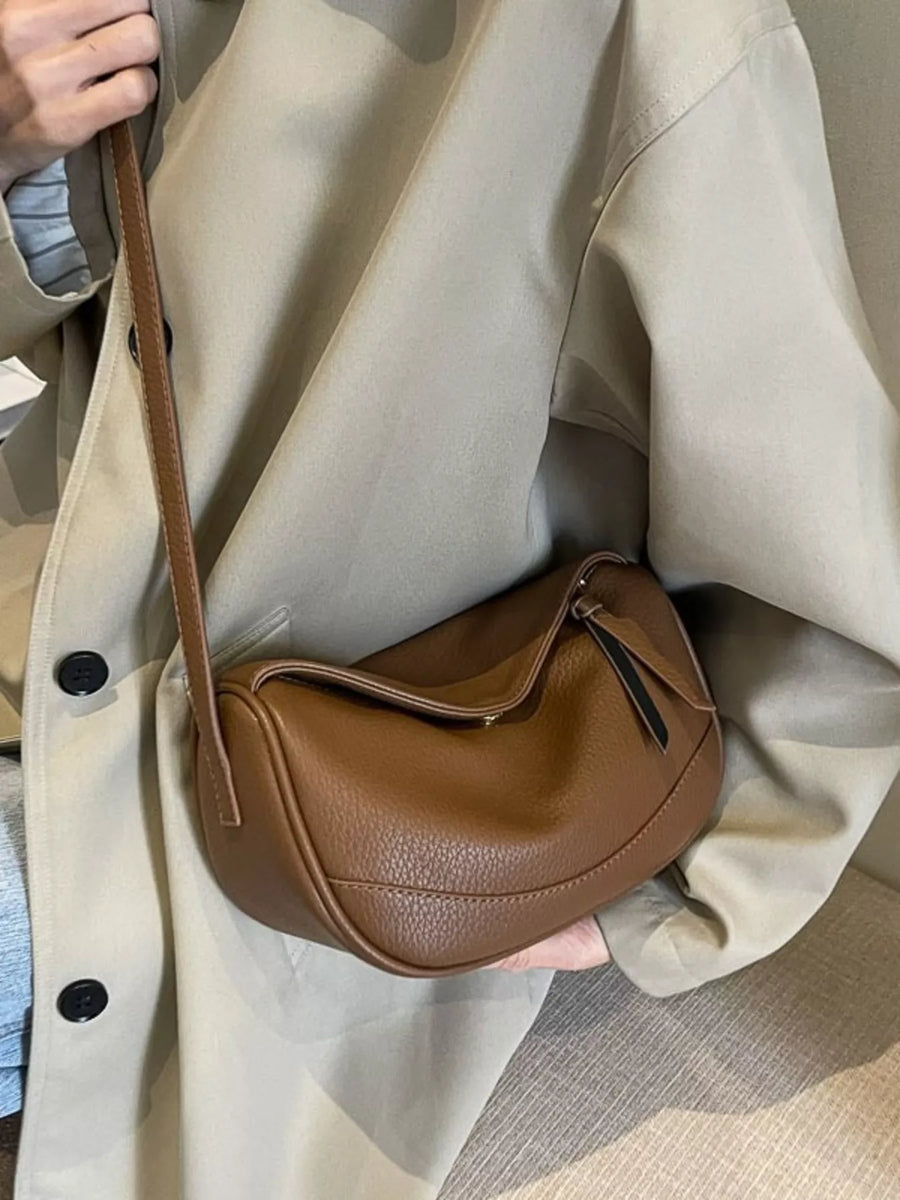 Brown leather minimalist crossbody bag with a curved shape and adjustable strap