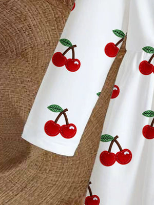 White baby dress with long sleeves and a red cherry print.