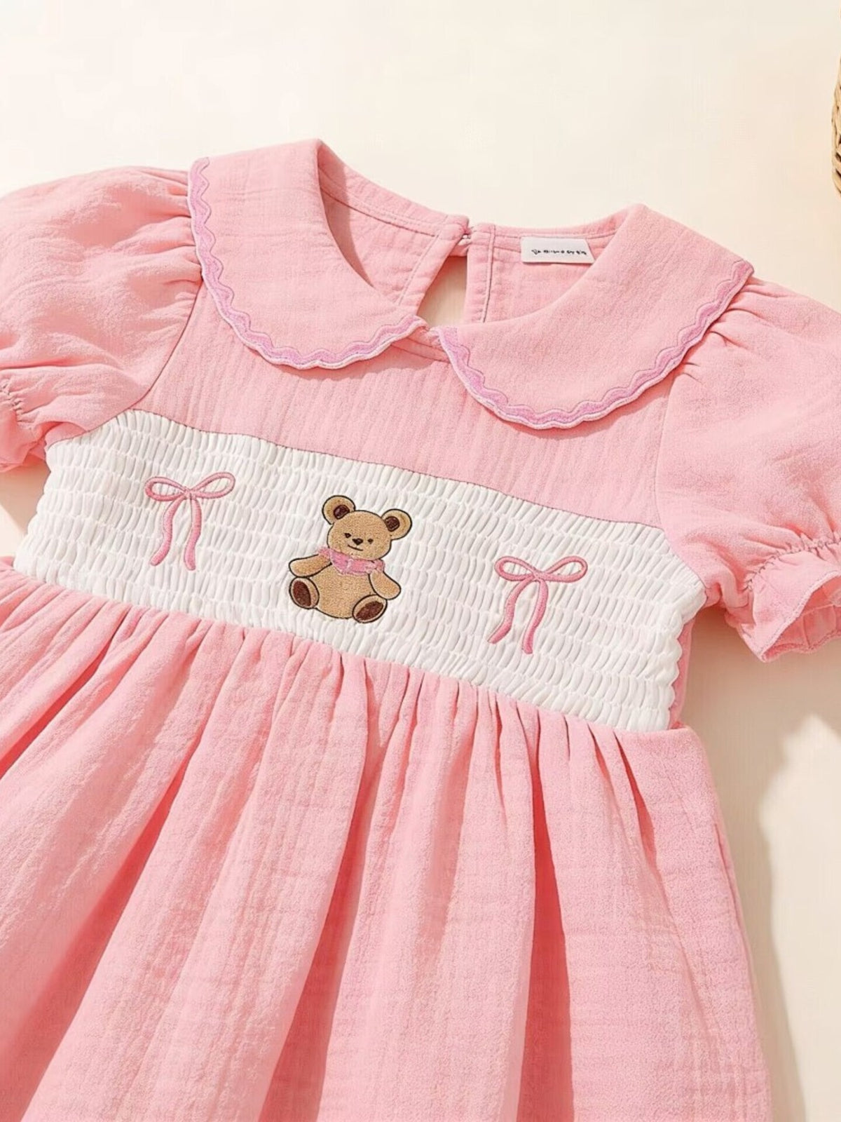 Pink baby dress with smocked bodice, teddy bear embroidery, and puff sleeves.
