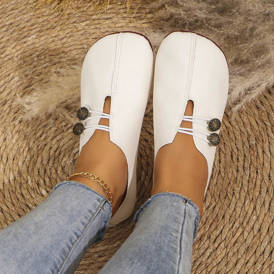 White leather slip-on flats with antique gold button detail and elastic straps.