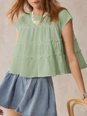 Green tiered ruffle blouse with short sleeves and a relaxed fit, styled with a denim skirt.