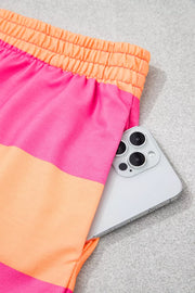 Vibrant striped drawstring shorts in pink and orange with a phone in the pocket.
