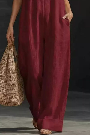 Burgundy halter-neck jumpsuit with pockets and wide legs, worn with sandals and a straw bag.