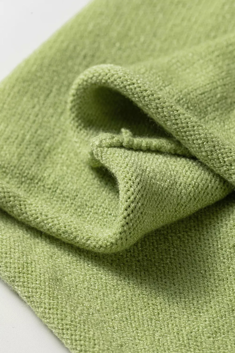 Light green knit sweater with a textured weave and folded hem detail.