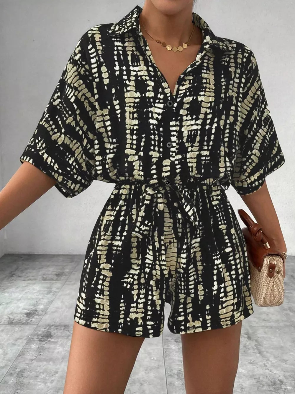 Black and cream abstract print belted romper with collared button-front top and short sleeves.