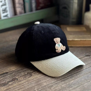 Black corduroy baseball cap with embroidered bear detail and light beige brim.