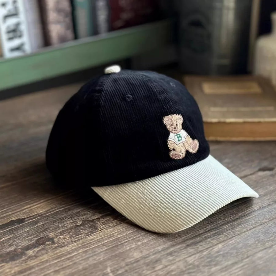 Black corduroy baseball cap with embroidered bear detail and light beige brim.