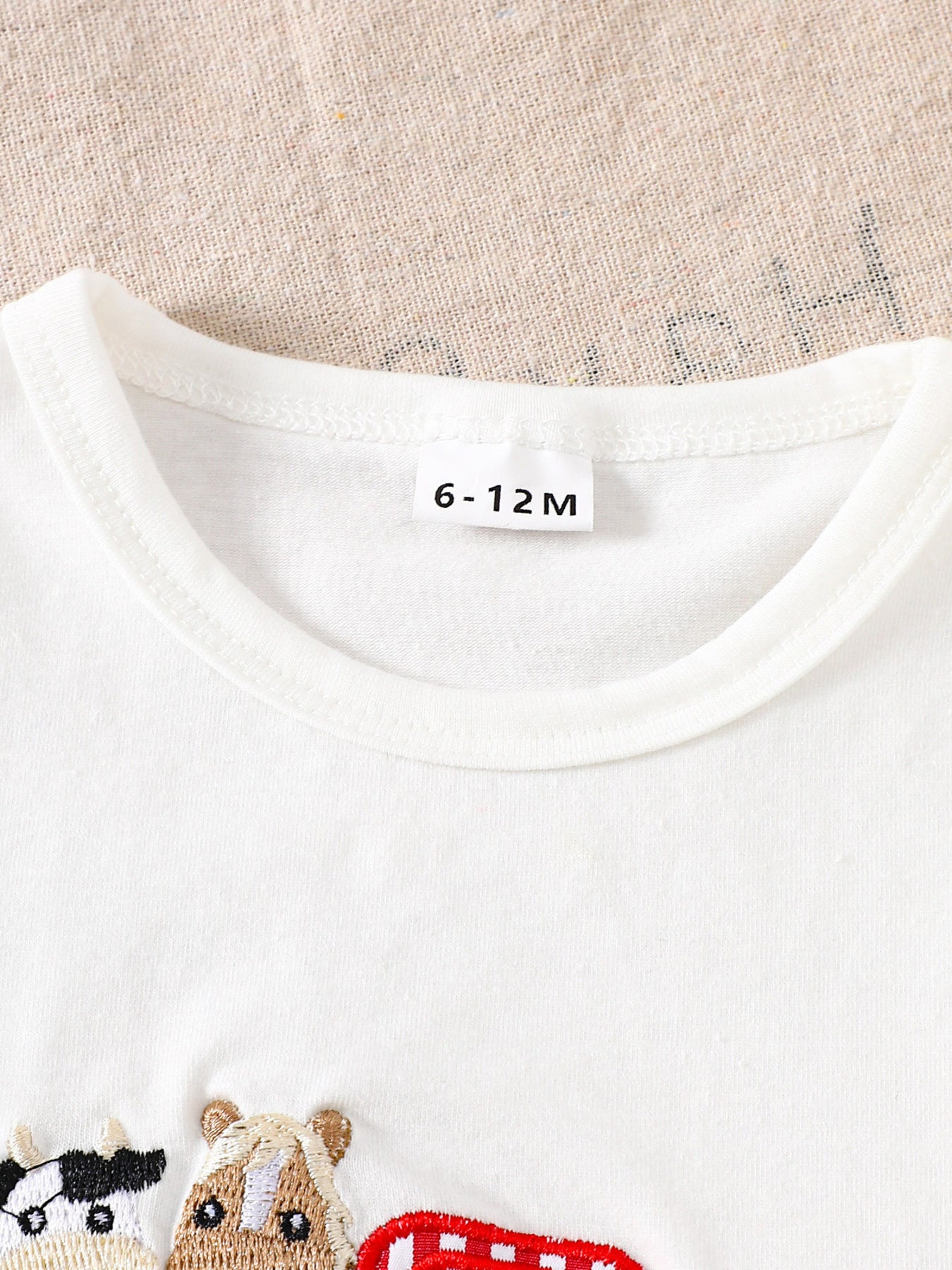 White baby tee with crew neck and embroidered farm animals and tractor detail.