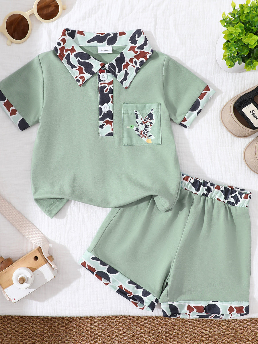 Sage green baby polo and shorts set with camouflage collar and trim, featuring a duck applique on the chest pocket.