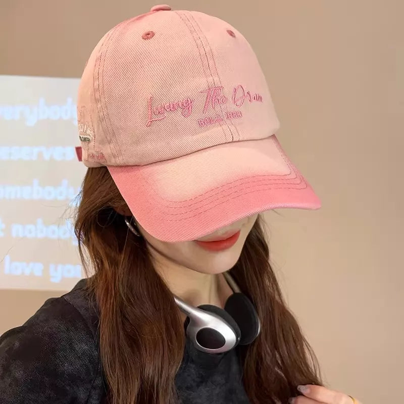 Washed pink cotton baseball cap with embroidered text and gradient detail.