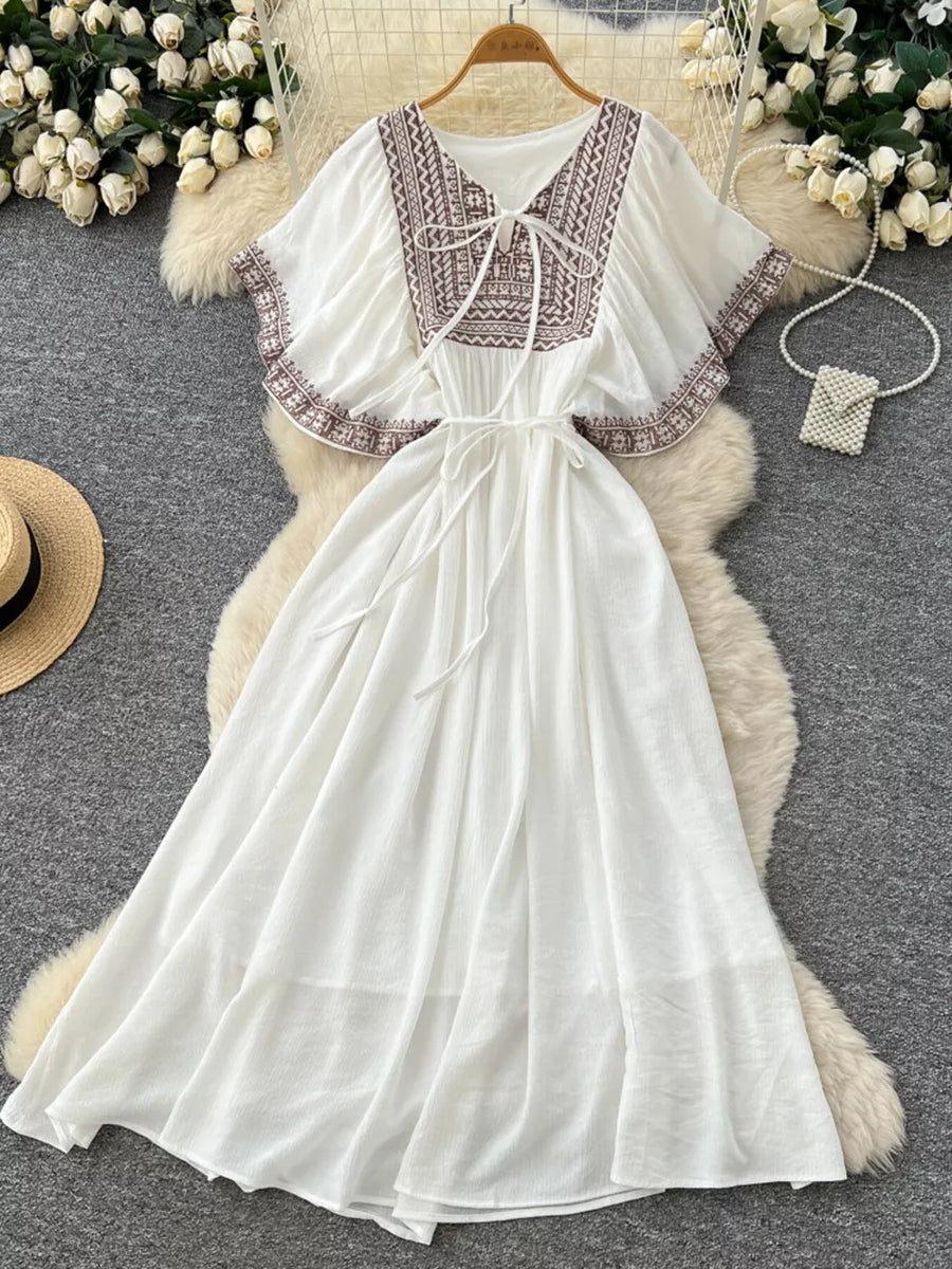 White embroidered V-neck maxi dress with tie detail and flutter sleeves.