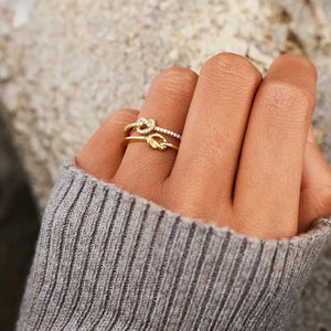 Gold knot rings, one plain, one pavé crystal band, stacked on a finger.