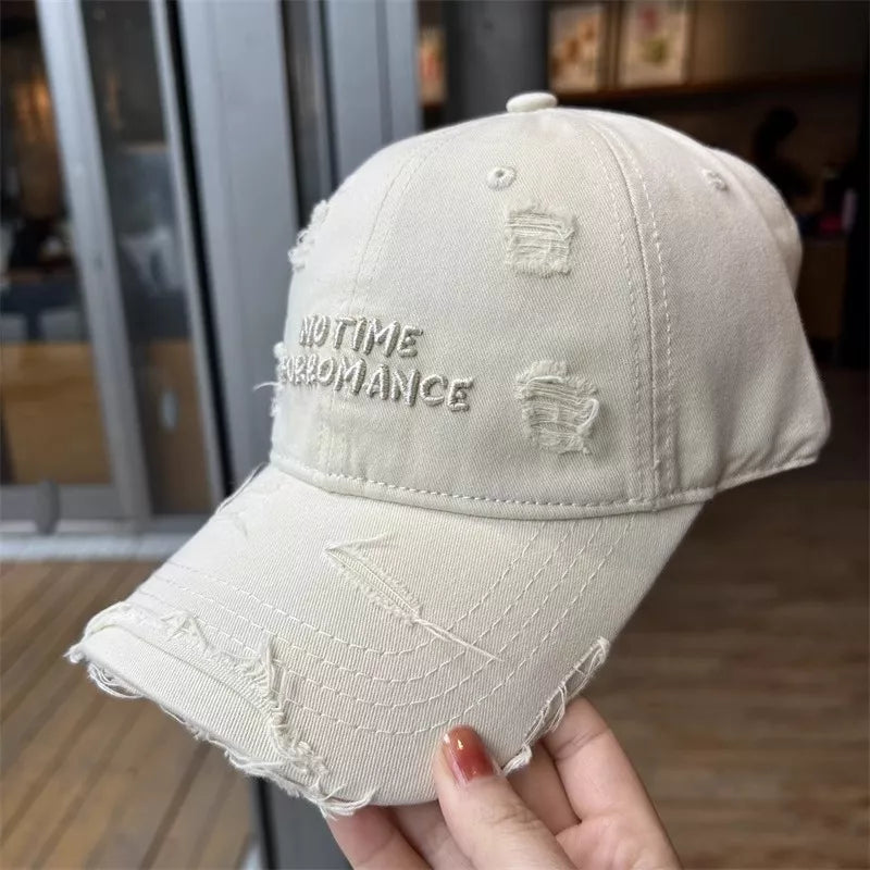 Beige distressed cotton baseball cap with embroidered text and frayed details.
