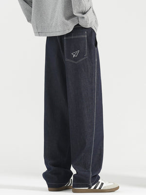 Men's dark wash wide-leg jeans with white stitching and paper airplane pocket detail.