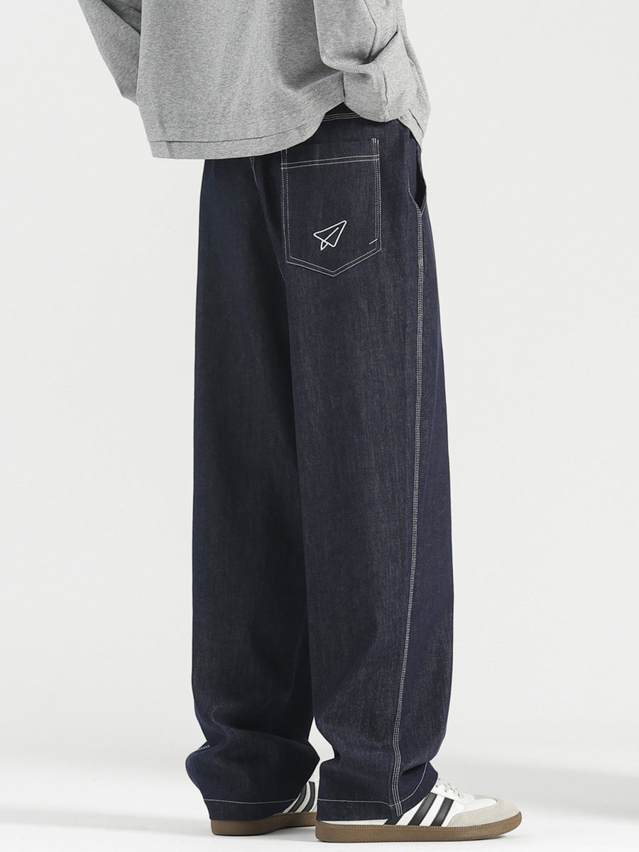 Men's dark wash wide-leg jeans with white stitching and paper airplane pocket detail.