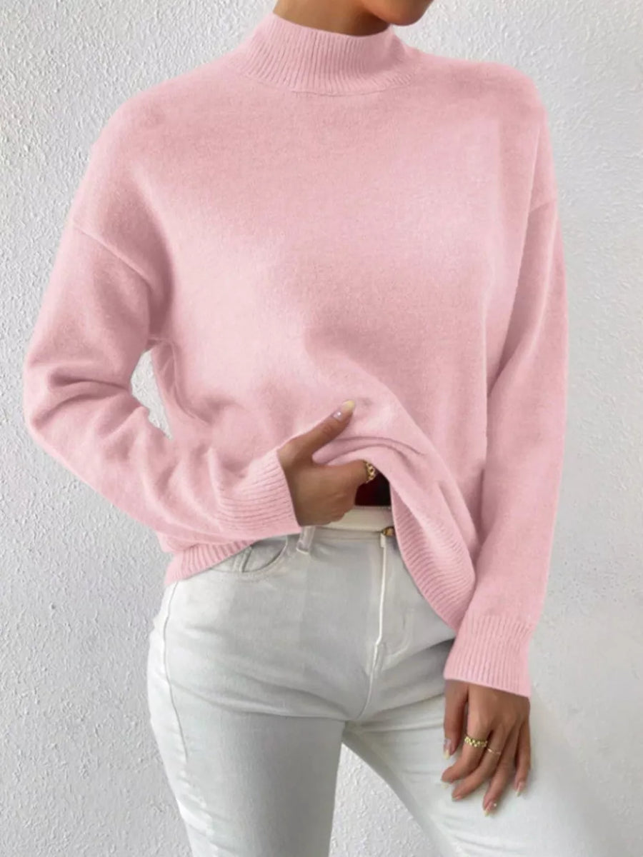 Pink mock neck knit sweater with dropped shoulders, styled with white jeans.