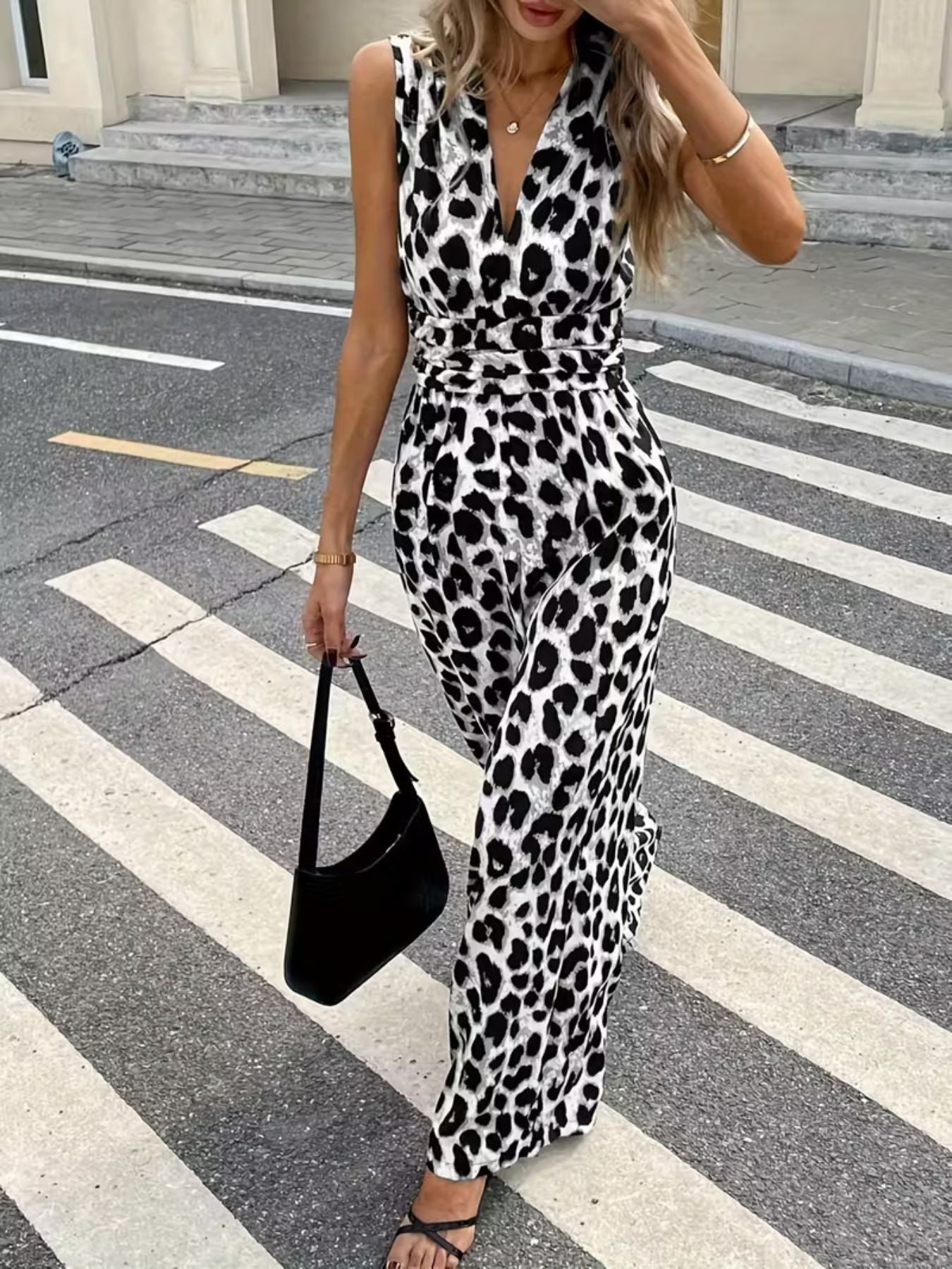 Sleeveless leopard print romper with V-neck and cinched waist, styled with a black shoulder bag.