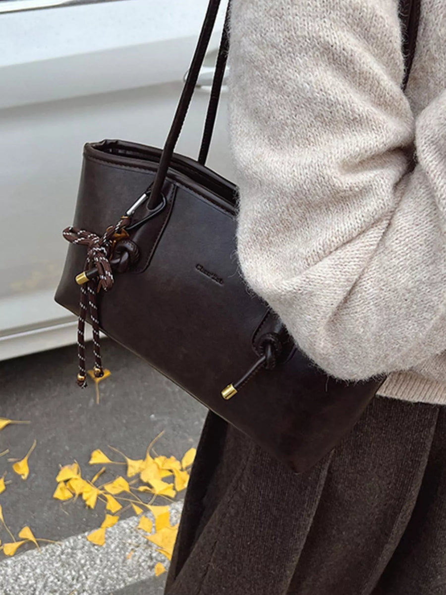 Brown leather shoulder bag with drawstring detail and gold hardware, worn with a cream sweater.