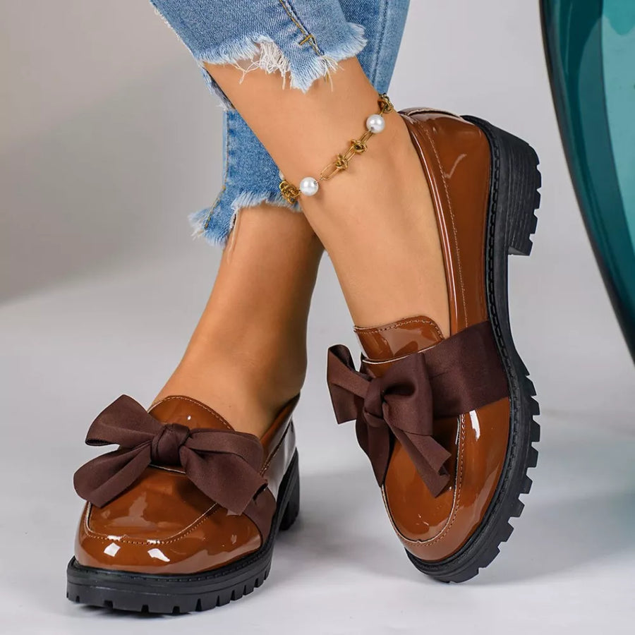 Brown patent loafers with large bow detail and lug sole.