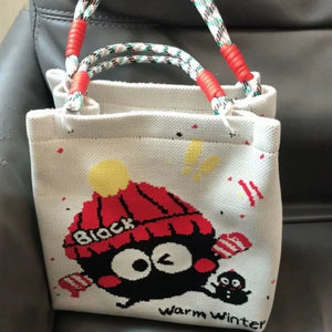 Cartoon graphic tote handbag in white with a black character wearing a red hat and mittens.
