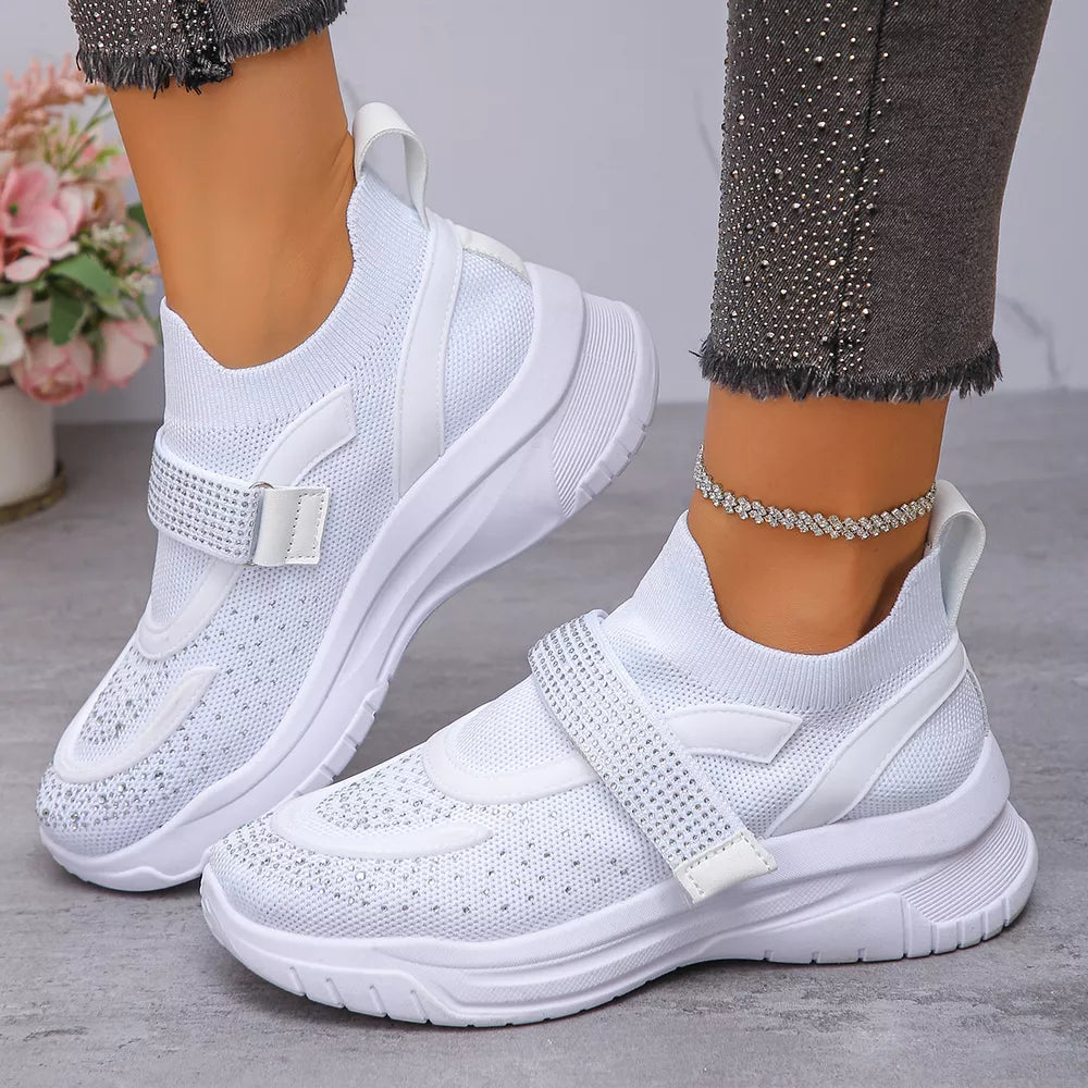 White mesh slip-on sneakers with adjustable rhinestone straps and cushioned soles.