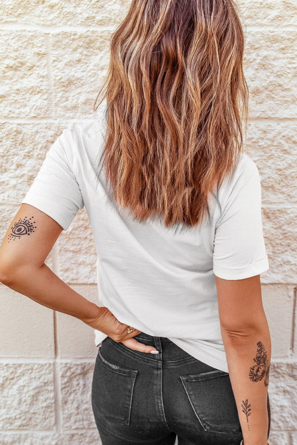 White graphic t-shirt with short sleeves and a round neckline, featuring a subtle eye design tattoo on the arm.