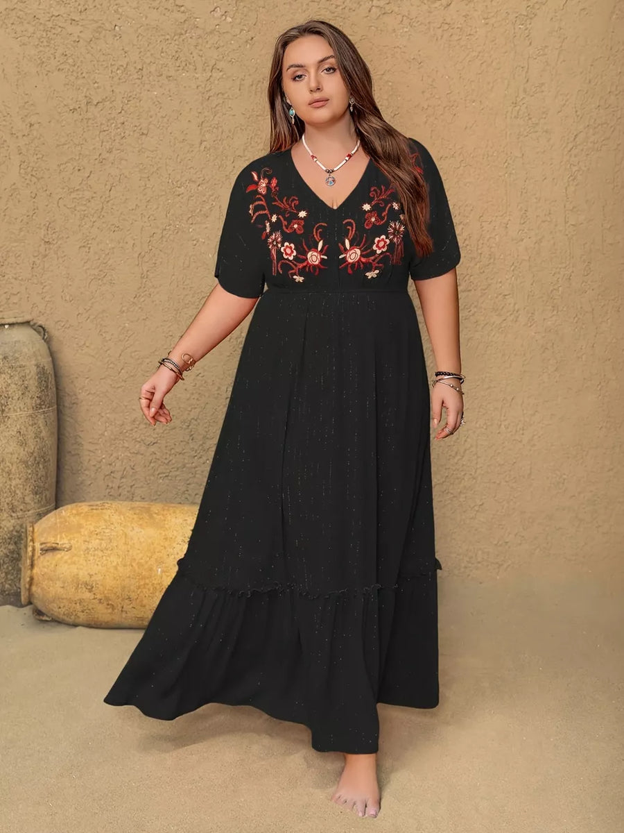 Black plus size maxi dress with V-neck, embroidered floral detail, short sleeves, and ruffled hem.