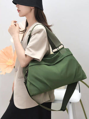 Green nylon duffel bag with adjustable strap, worn by a woman in a beige blazer and black bucket hat.