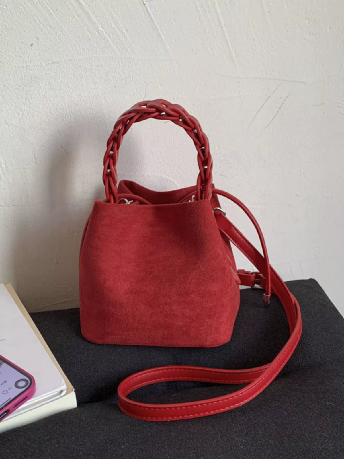 Red suede mini bucket bag with braided top handle and crossbody strap.