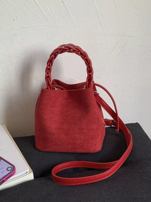 Red suede mini bucket bag with braided top handle and crossbody strap.