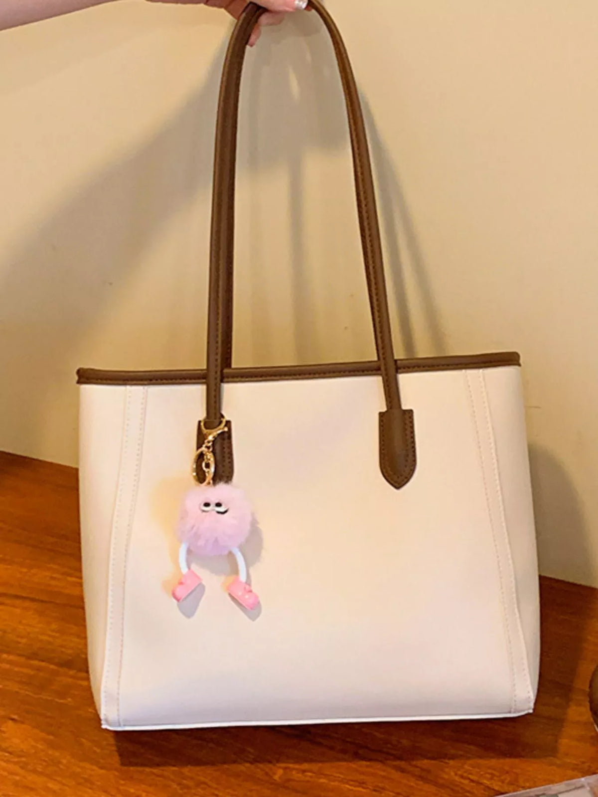 Sophisticated beige PU leather tote bag with brown trim and a fluffy pink charm.