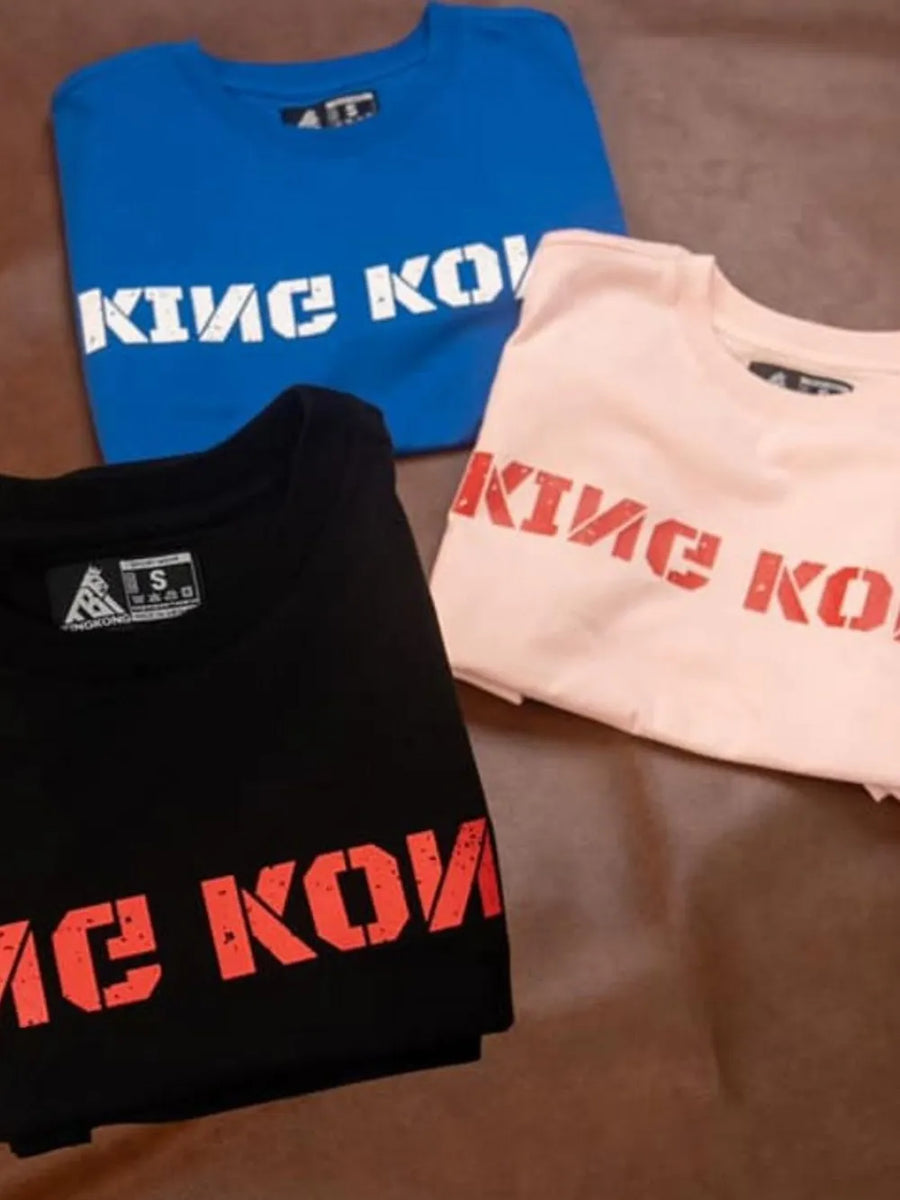 King Kong graphic tees in black, blue, and dusty pink with bold stencil lettering.