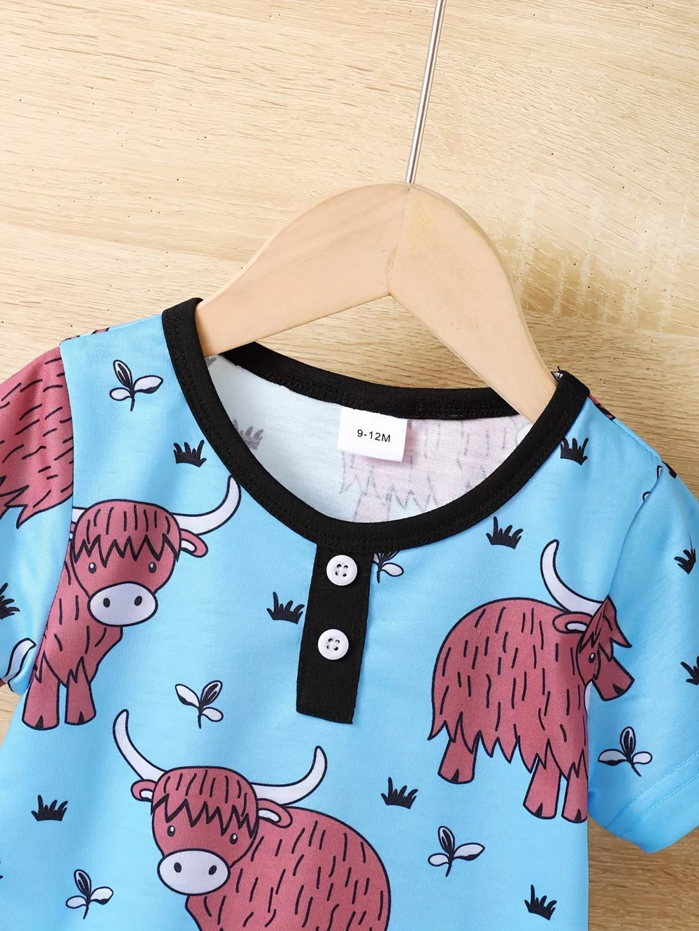 Baby pajama set with highland cow print on light blue, black trim, henley neckline, short sleeves.