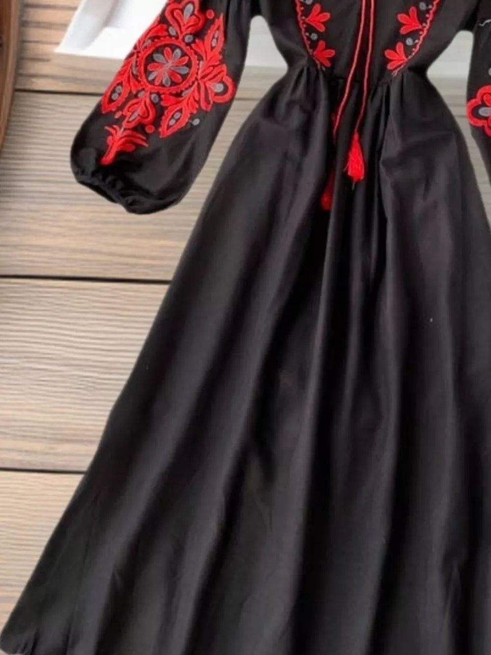 Black maxi dress with red embroidery on balloon sleeves and neckline, featuring tassels.