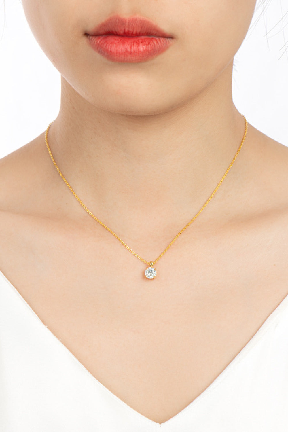 Gold chain necklace with a single clear solitaire pendant, worn by a woman.