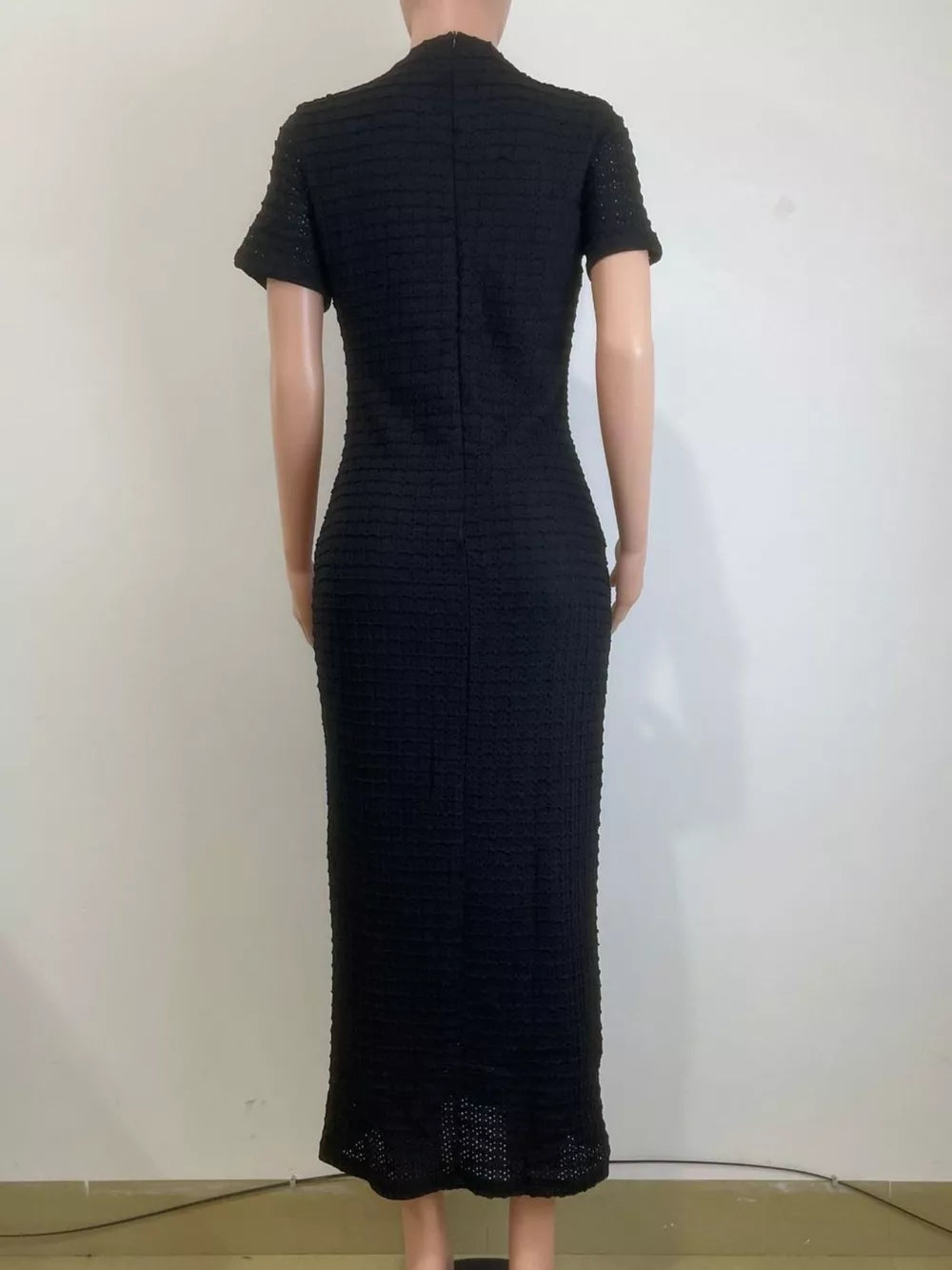 Black textured midi dress with short sleeves and a high neckline, featuring a subtle gold button detail.