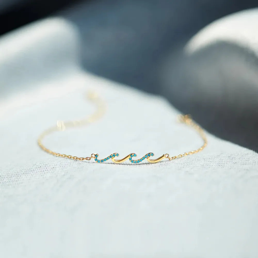 Gold wave bracelet with turquoise zirconia accents on a delicate chain.